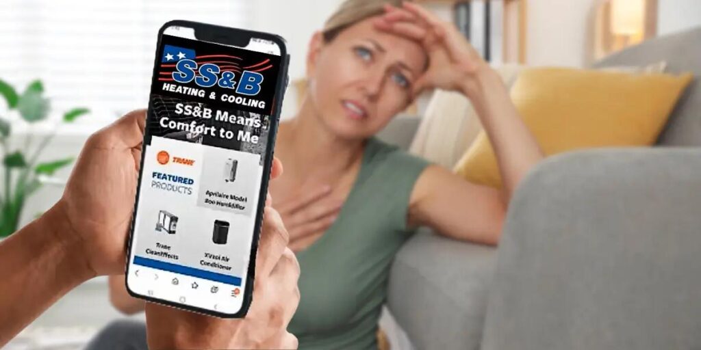A person looking distressed in a warm home while someone browses the SS&B Heating & Cooling website on a smartphone, searching for HVAC solutions.